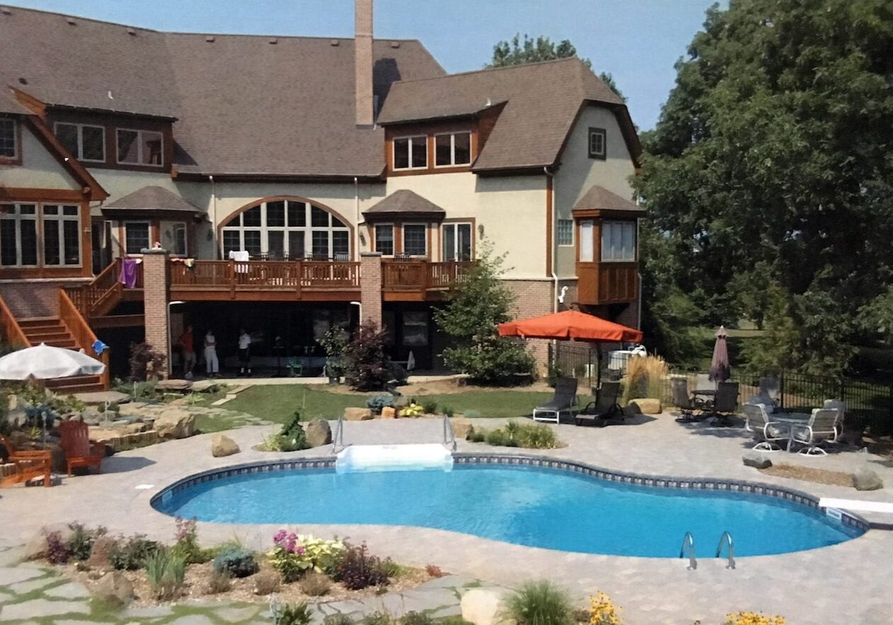 A large pool with a fountain and a house in the background.